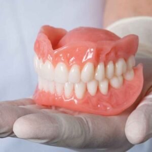 Primer plano de dentadura postiza completa sostenida por una mano con guantes de látex.